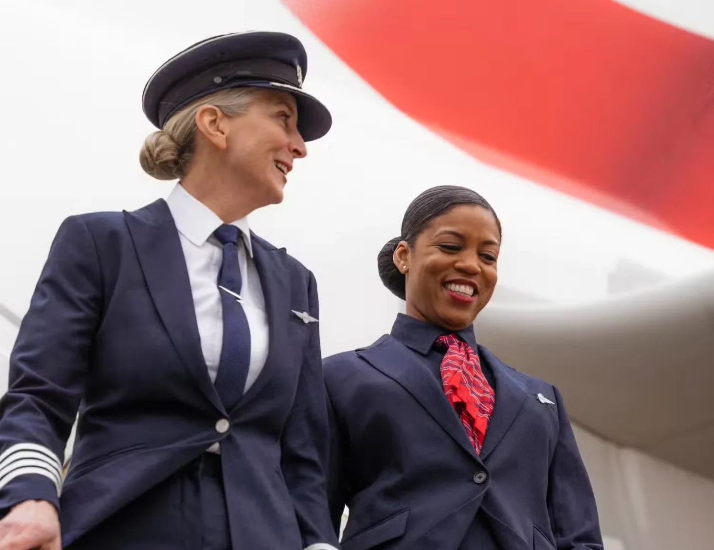 Two women in uniform stand proudly beside an airplane, showcasing their dedication and professionalism in aviation.
